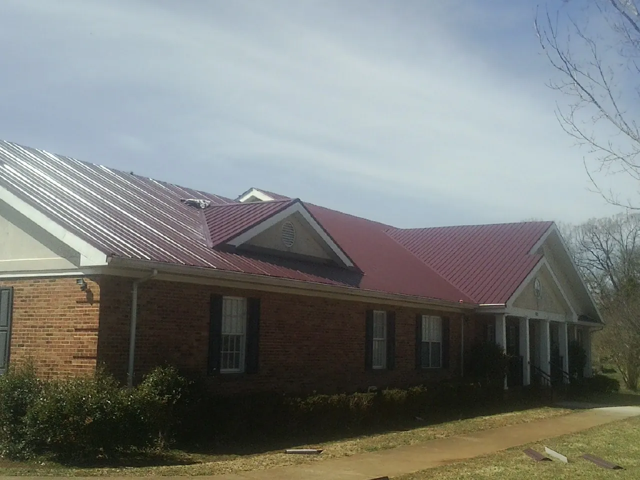 Red metal roof with gabled entries on a long brick building, from a Hail Damage Roof Repair job in Indiahoma