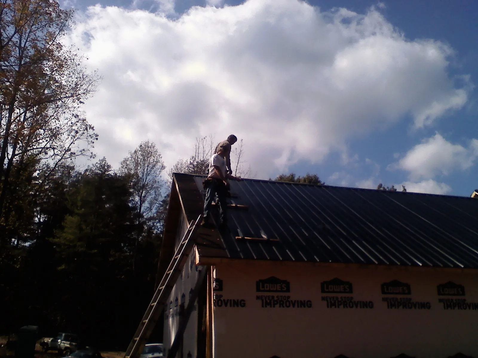 Roofer fastening dark metal panels high against a cloudy sky, from a Roof Inspection job in Indiahoma