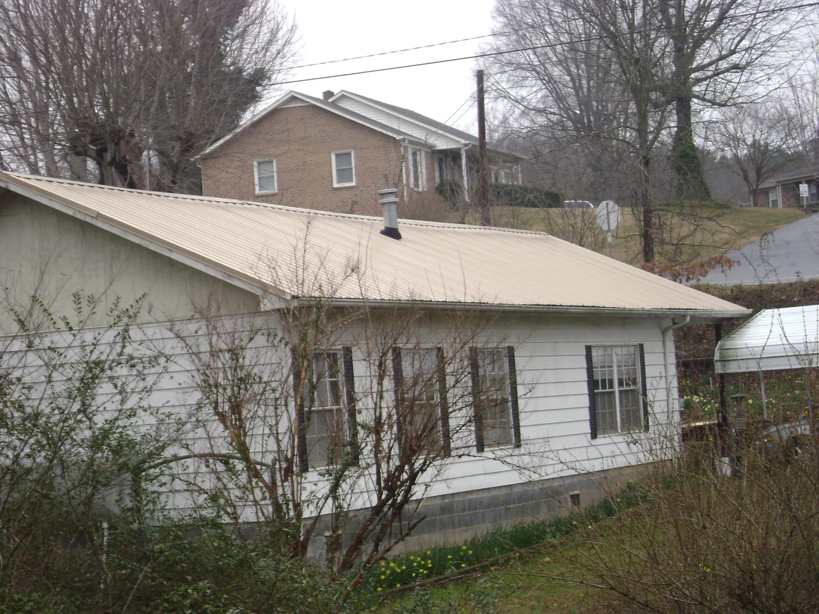 Tan metal roof on a white sided house set into a hillside — Commercial Roofing by Roofing Brothers in Indiahoma