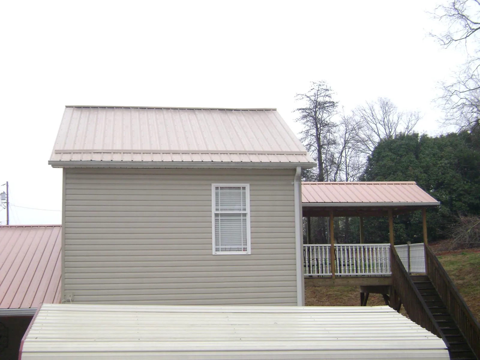 Tan metal roofs on a two story addition and attached porch, from a Roof Replacement job in Indiahoma